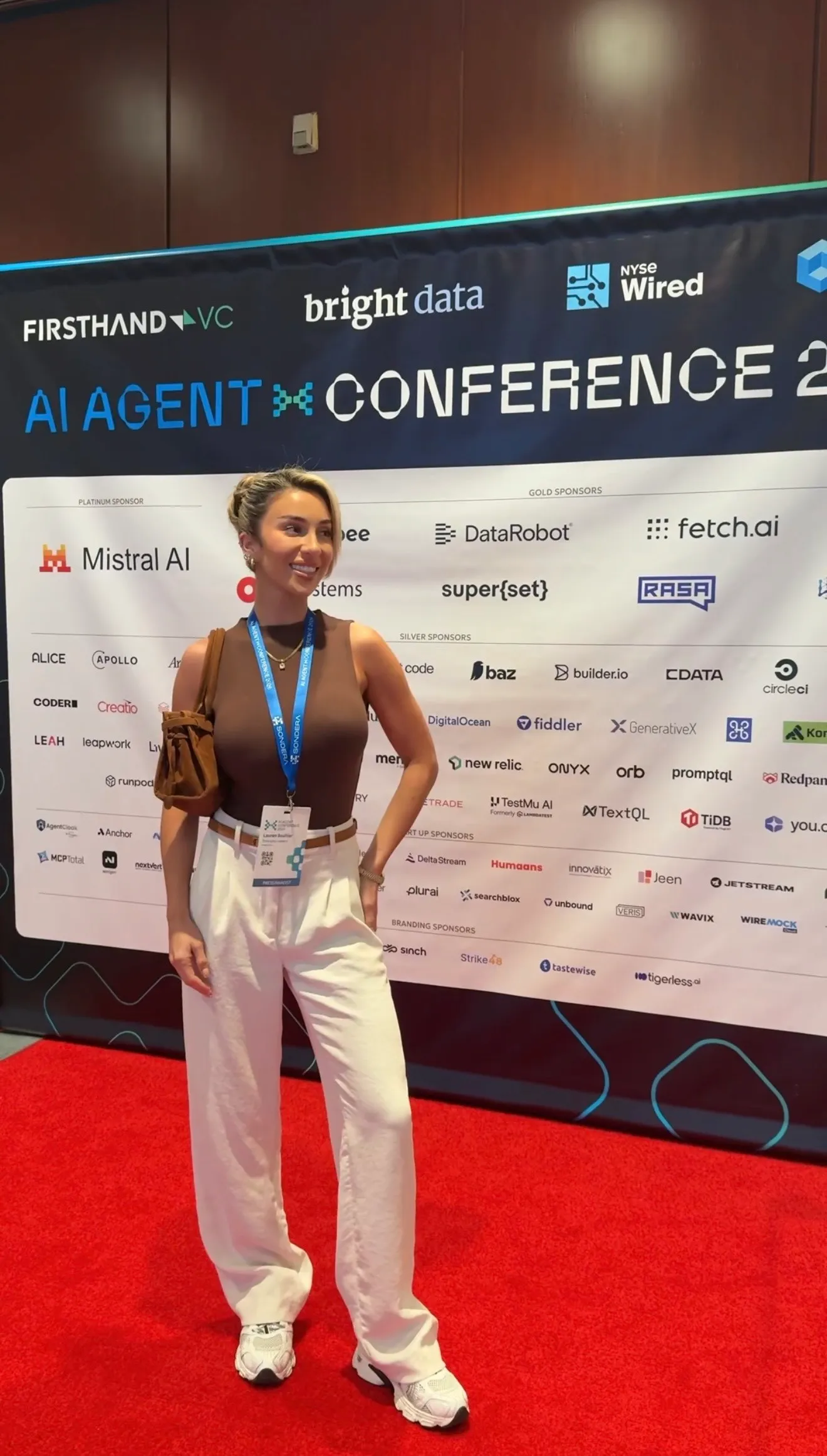 Lauren at the AI Agent Conference, standing in front of the sponsor step-and-repeat.